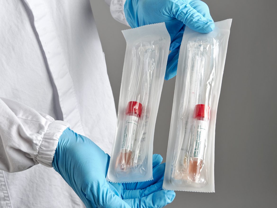 COVID-19 Test Packages with Swabs and Tubes Being Held By Gloved Hands